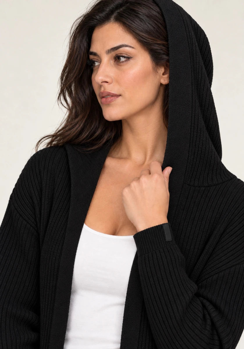 Close-up of a model wearing ELLY's black ribbed cardigan with the hood raised, showing the ribbed sleeve and open front.