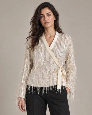 Close-up of the Cassandra Panna fringe wrap jacket showing its V-neck, side tie and hanging fringe, worn with black trousers.