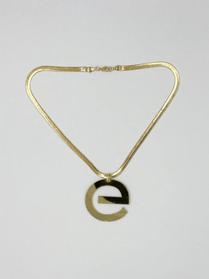 Gold-tone necklace laid flat, showing a broad flat chain, clasp and large lowercase e-shaped pendant.