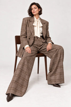 Rosalinda brown check blazer and matching Hope wide-leg trousers shown seated, styled with an ivory bow-neck blouse.