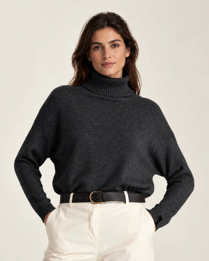 Front view of Maglia Collo Alto Nero dark knit sweater with a ribbed turtleneck and cuffs, worn with cream trousers