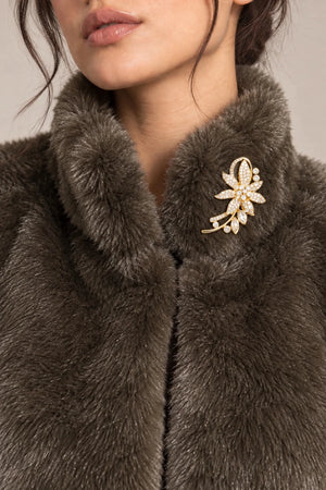 Detail of the raised collar on the brown Mora Moro plush jacket, shown with a gold-tone floral brooch with pale stones.