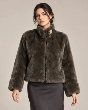 Close-up of the brown Mora Moro plush jacket with a gold-tone floral brooch at the collar, styled with a charcoal skirt.