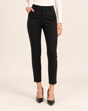 Front detail of black tailored ankle-length trousers showing the waistband and pockets, with one hand in a pocket.