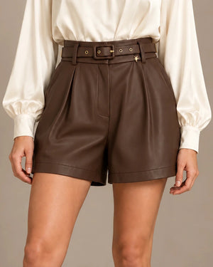 Close-up front view of brown leather-look shorts with front pleats, a matching belt and a star charm.