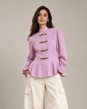 Close-up of the pink Regina check peplum shirt showing its decorative frog closures, peplum hem and ruffled cuffs.