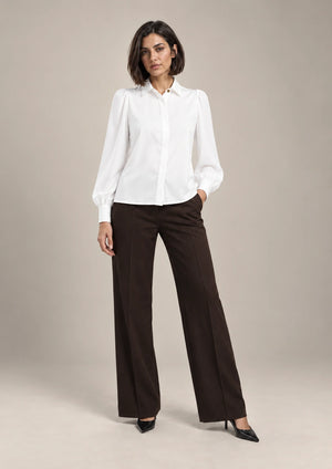 Full-length styling view of the white Serena shirt with a pointed collar and long puff sleeves, worn with brown wide-leg trousers.