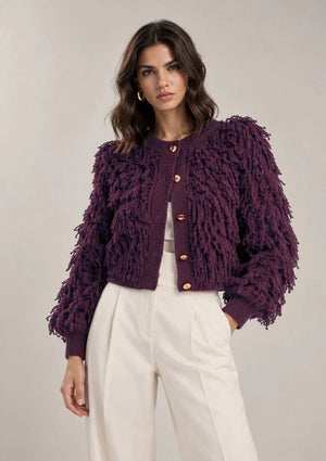 Front view of the Viola cardigan with a fringe-textured surface, round neckline, gold-tone buttons and ribbed trim, worn with ivory trousers.