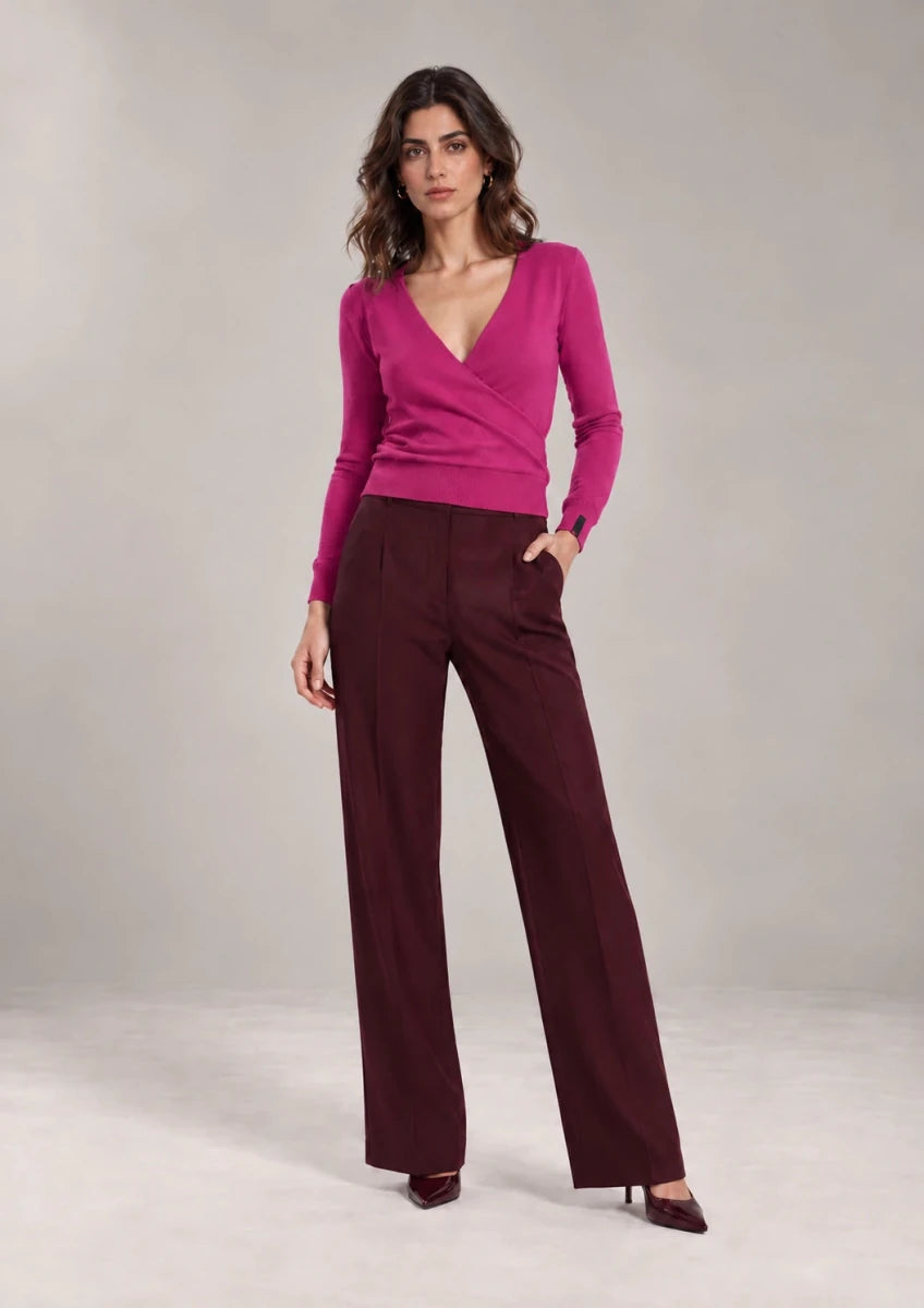Full-length styling view of the Alba Malva sweater with a wrap-effect V-neck front and long sleeves, worn with burgundy trousers.