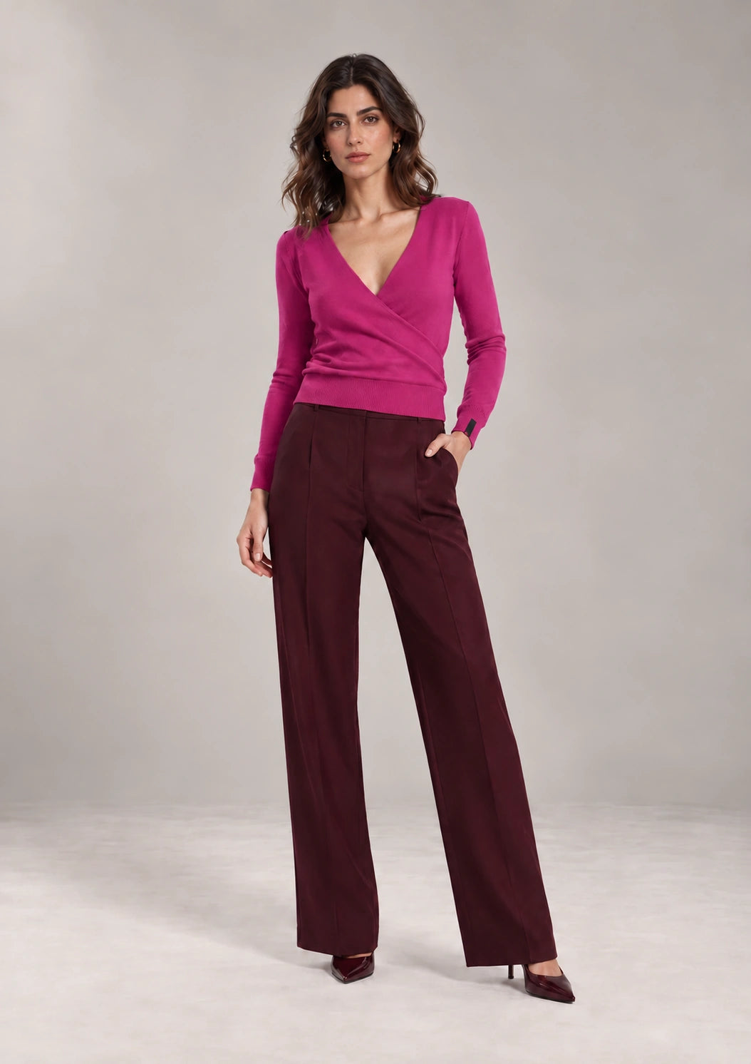 Full-length styling view of the Alba Malva sweater with a wrap-effect V-neck front and long sleeves, worn with burgundy trousers.