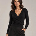 Close-up of the black Alba sweater showing its crossover V-neck, long sleeves and ribbed hem.