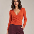 Close-up of the orange Alba Arancione sweater showing the crossover V-neck front, long sleeves and ribbed hem.