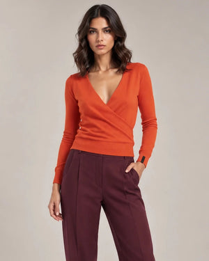 Front styling view of the orange Alba Arancione sweater with a wrap-effect V-neck and long sleeves, worn with burgundy trousers.