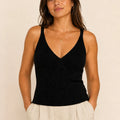 Woman wearing a black ribbed knit V-neck top with wide shoulder straps and ivory trousers.
