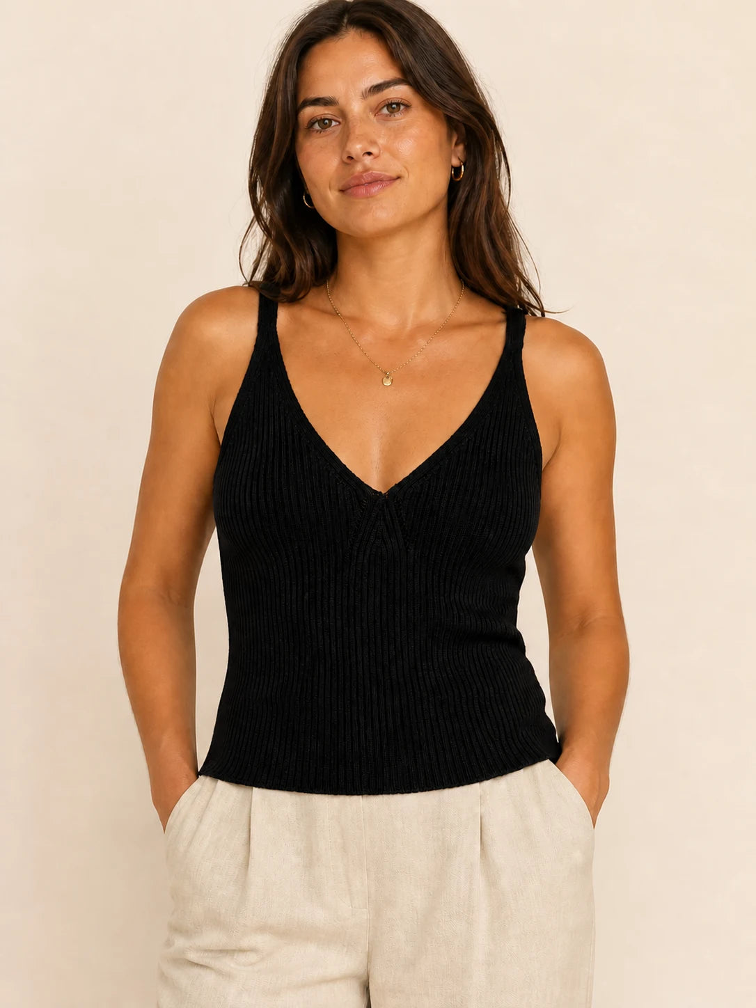 Woman wearing a black ribbed knit V-neck top with wide shoulder straps and ivory trousers.