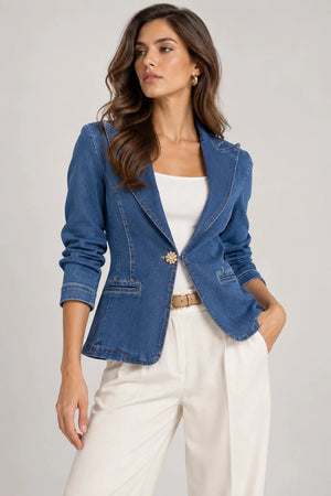 Three-quarter front view of a model wearing a blue denim tailored blazer with a white top and ivory trousers.