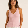 Woman wearing a blush pink ribbed knit V-neck top with wide shoulder straps and ivory trousers.