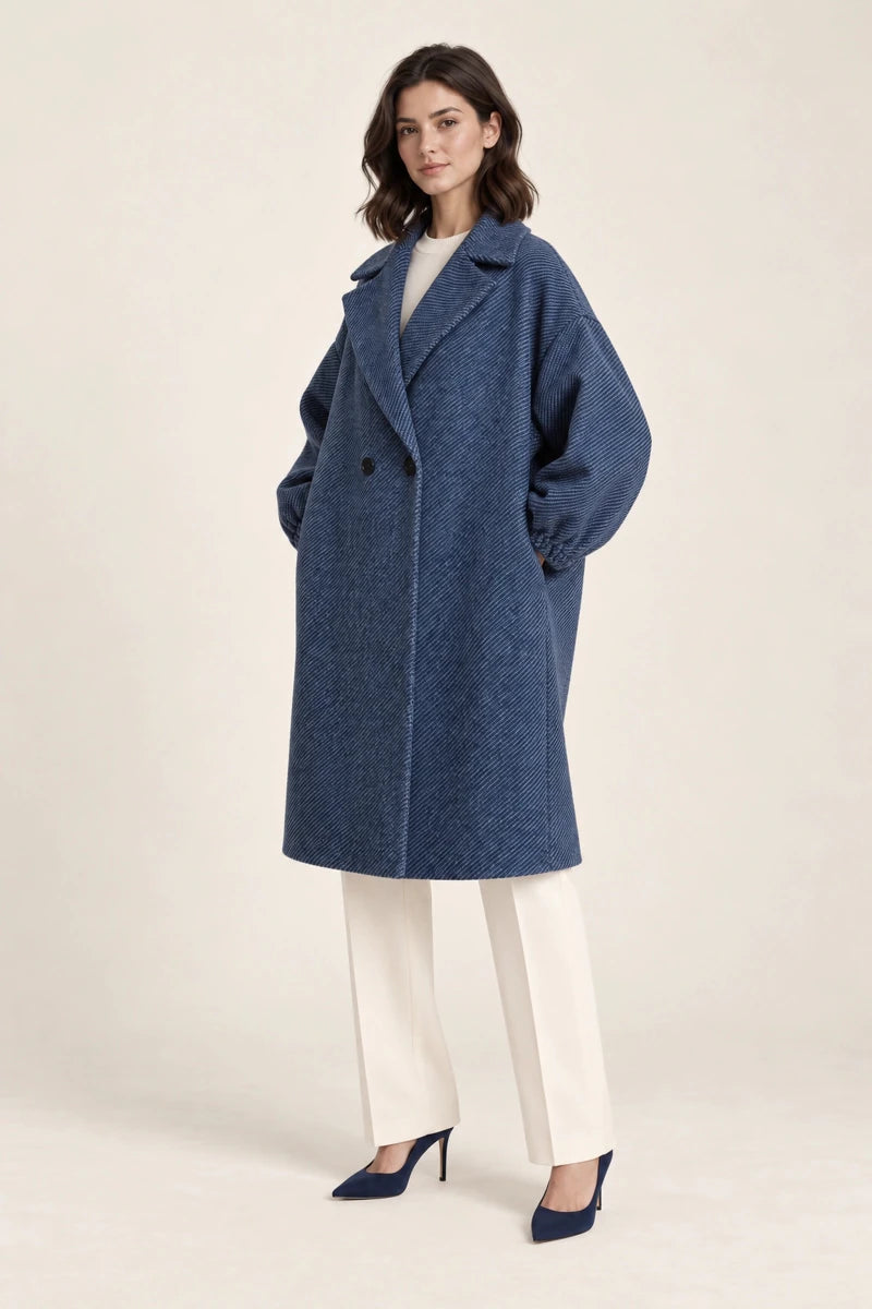 Three-quarter view of Cappotto Oversize Blu/Nero, a blue double-breasted coat with wide sleeves, worn with ivory trousers and navy heels.