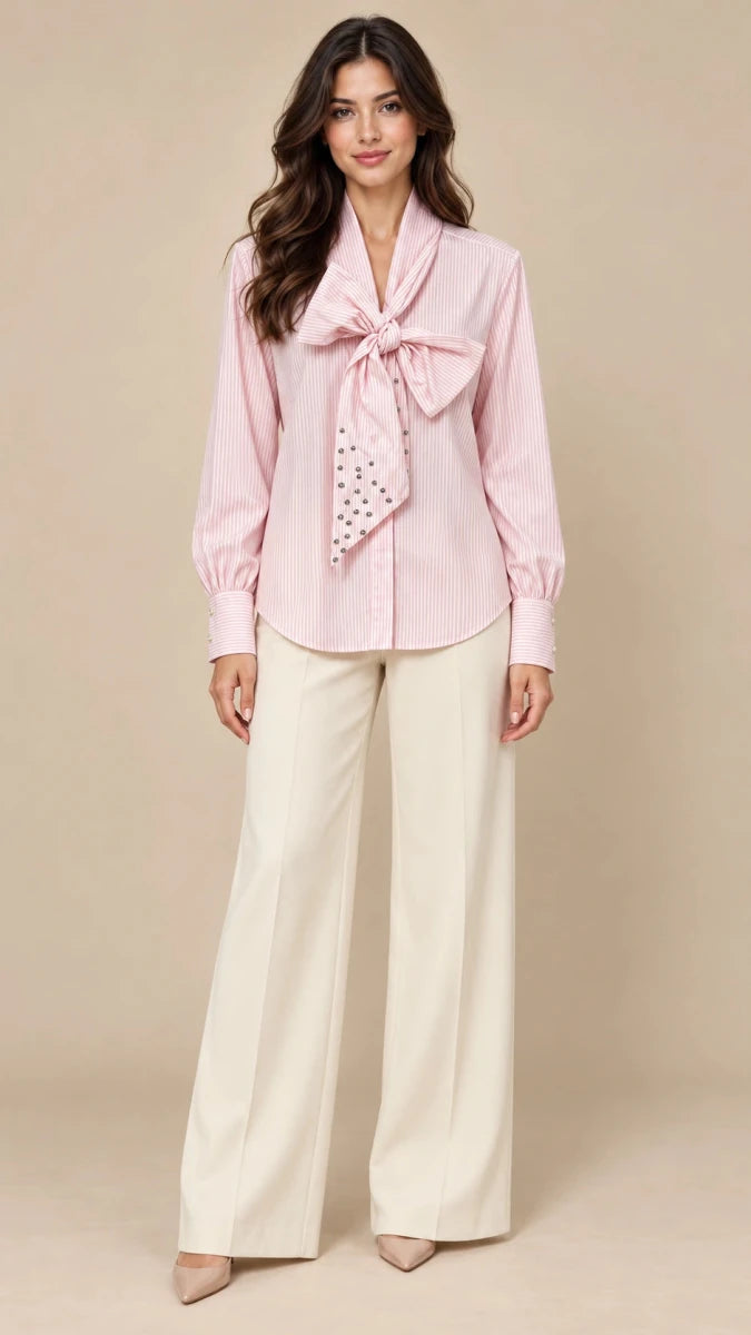 Full-length styling view of the Carola pink striped bow shirt worn with ivory wide-leg trousers.