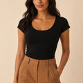 Black scoop-neck cap-sleeve top tucked into camel trousers, front view