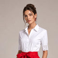 White button-front shirt with crystal-embellished cuffs, worn with a red bow-waist skirt, front view