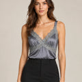 Close-up of the grey Domitilla camisole with lace-trimmed V-neck, tucked into black trousers.