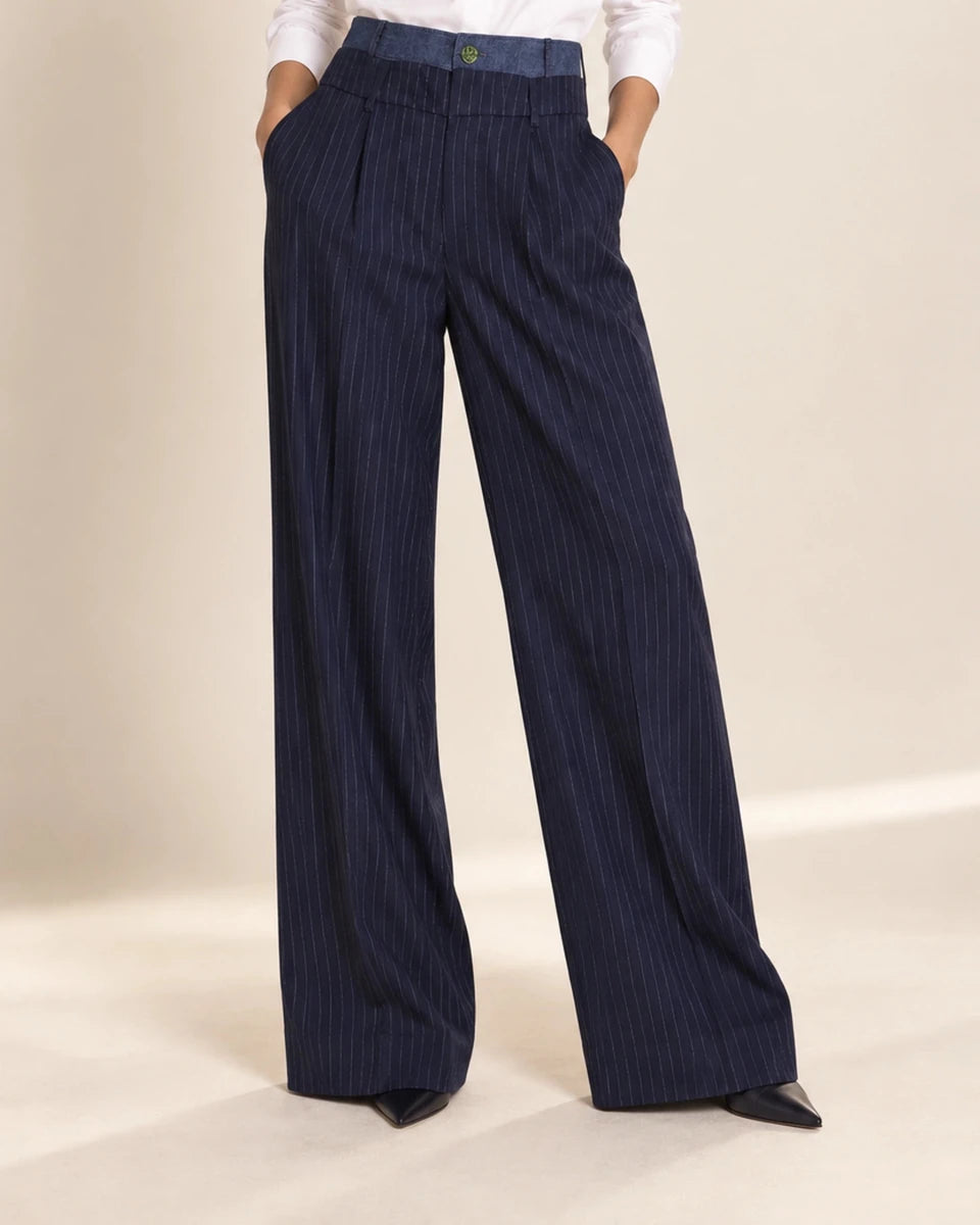 Close-up of Fiorella navy pinstripe trousers showing the contrast waistband, front pleats and wide legs.