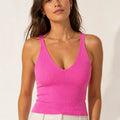 Woman wearing a bright fuchsia ribbed knit V-neck crop top with wide shoulder straps and ivory trousers.