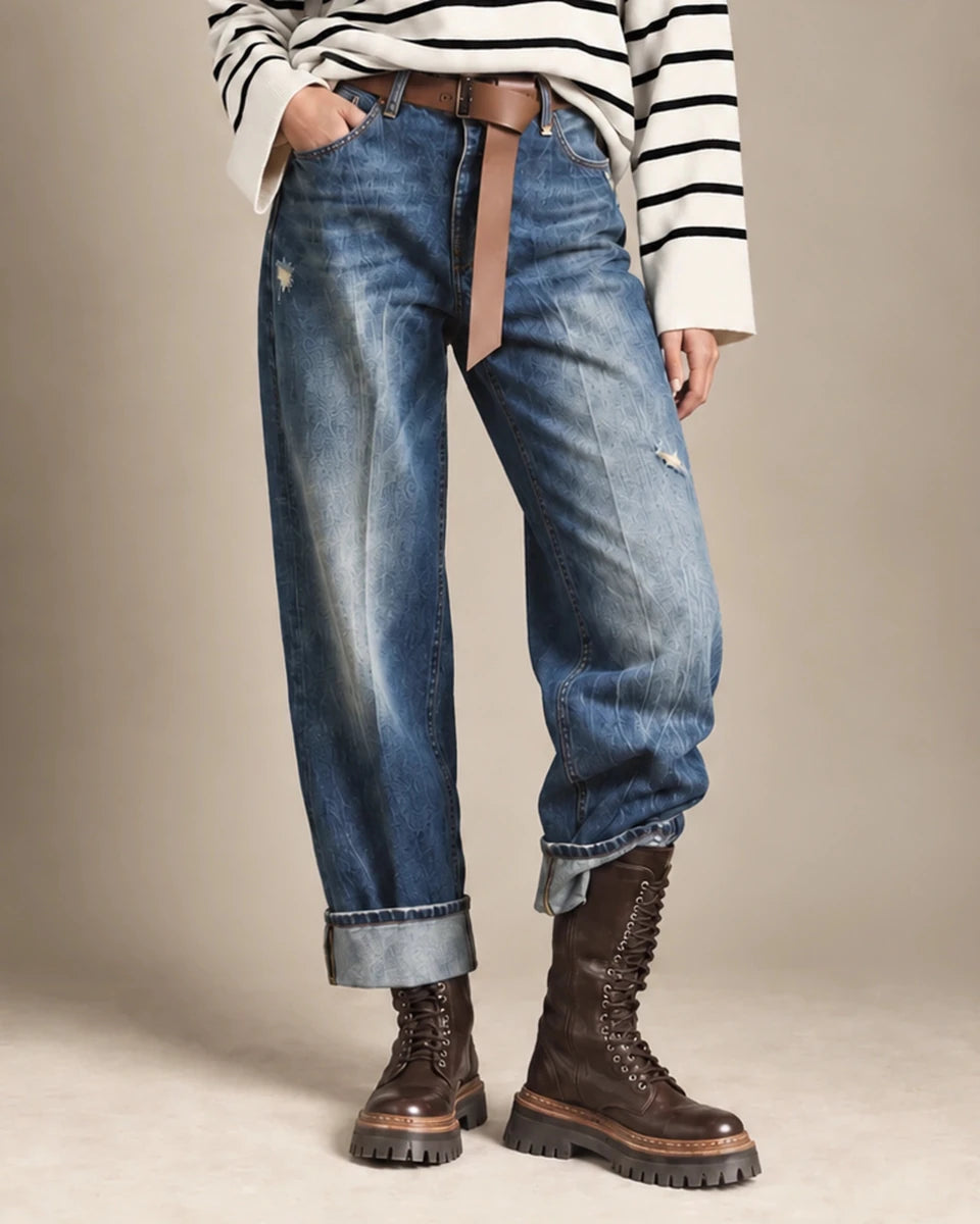 Harper blue relaxed jeans with turned-up cuffs and distressed details, styled with a brown belt and lace-up boots.