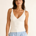 Woman wearing an ivory ribbed knit V-neck top with wide shoulder straps and light blue trousers.