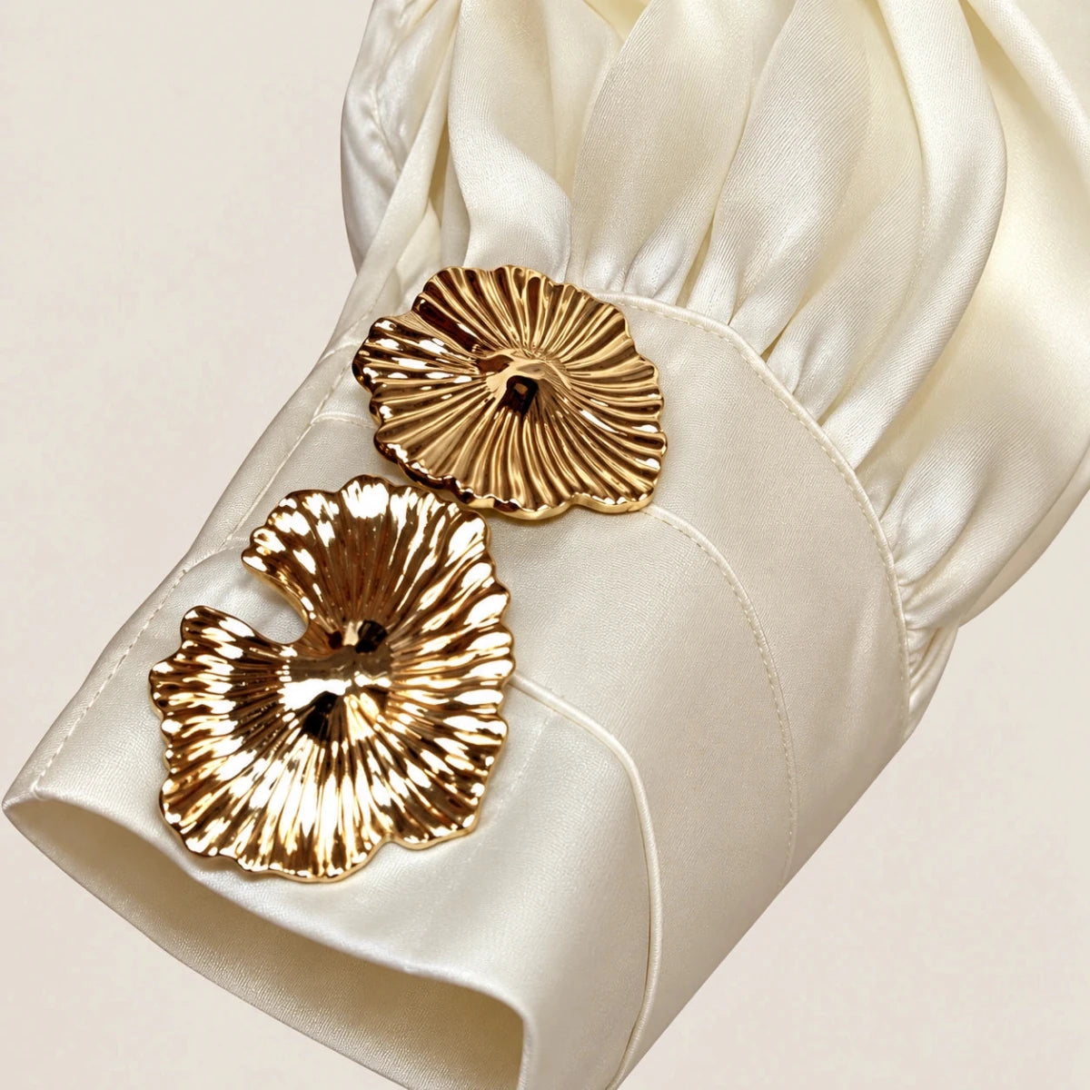 Close-up of the ivory Loredana Panna Bow-Neck Shirt cuff with two gold-tone floral buttons and gathered sleeve fabric.