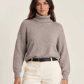 Front view of Maglia Collo Alto Greige sweater with a ribbed turtleneck and cuffs, worn with cream trousers