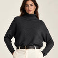 Front view of Maglia Collo Alto Nero dark knit sweater with a ribbed turtleneck and cuffs, worn with cream trousers