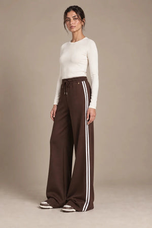 Full-length view of Mara Moro wide-leg track pants with a drawstring waistband and white side stripes, styled with an ivory top.