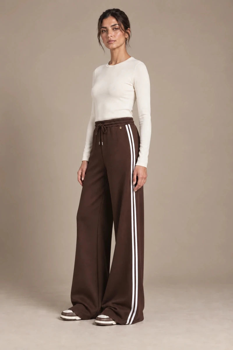 Full-length view of Mara Moro wide-leg track pants with a drawstring waistband and white side stripes, styled with an ivory top.