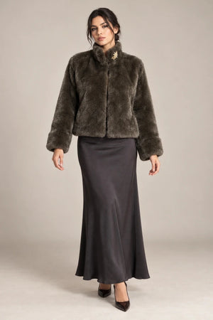 Full-length styling view of the brown Mora Moro plush jacket with a raised collar and wide turned-back cuffs, worn with a charcoal skirt.