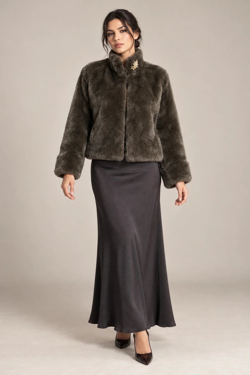 Full-length styling view of the brown Mora Moro plush jacket with a raised collar and wide turned-back cuffs, worn with a charcoal skirt.