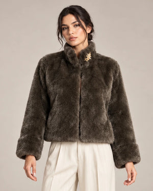 Close-up of the brown Mora Moro plush jacket showing its raised collar, long sleeves and wide cuffs, styled with ivory trousers.
