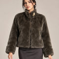 Close-up of the brown Mora Moro plush jacket with a gold-tone floral brooch at the collar, styled with a charcoal skirt.