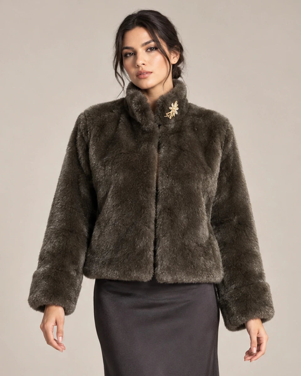 Close-up of the brown Mora Moro plush jacket with a gold-tone floral brooch at the collar, styled with a charcoal skirt.