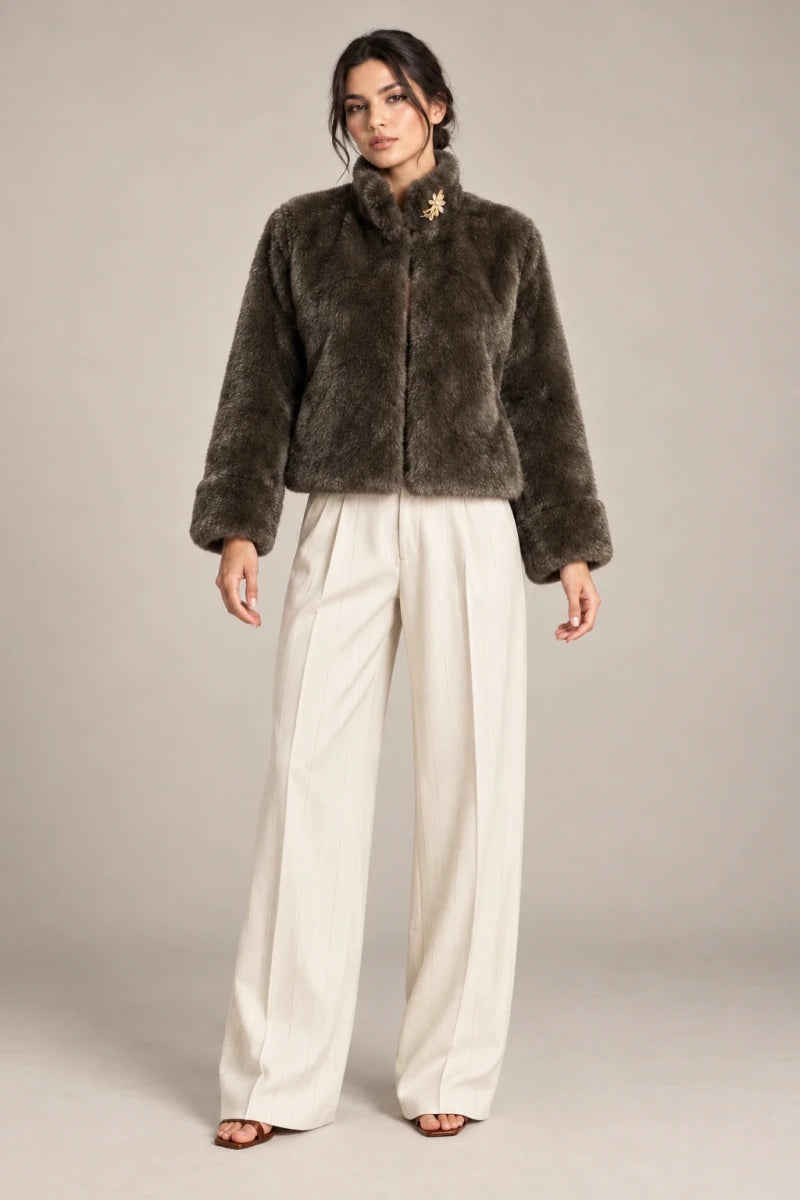 Full-length styling view of the brown Mora Moro plush jacket with a raised collar and wide turned-back cuffs, worn with ivory trousers.