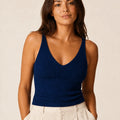Woman wearing the ELLY navy blue ribbed knit V-neck top with wide shoulder straps and ivory tailored trousers.