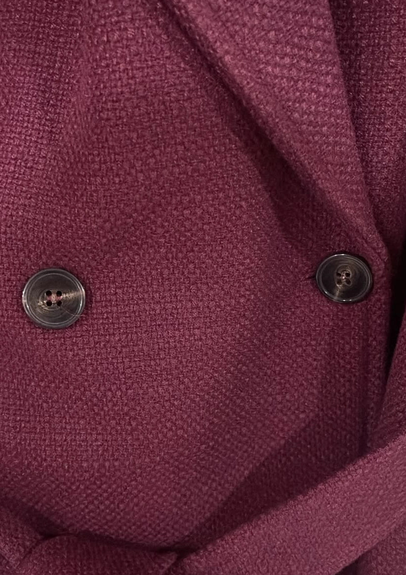 Close-up of the Persia Bordeaux coat showing its textured surface, lapel, dark buttons and waist belt.