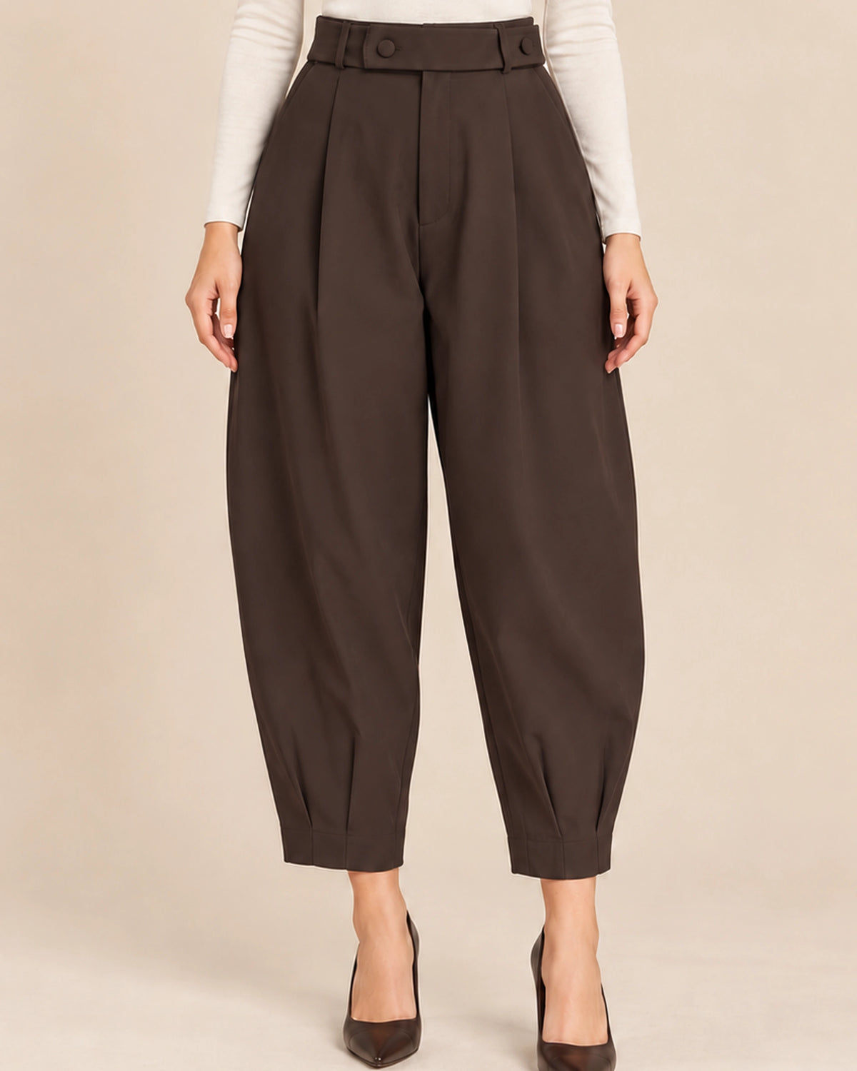 Front detail of deep brown Queen barrel-leg trousers with a wide button-detail waistband, front pleats and pleated ankle hems.
