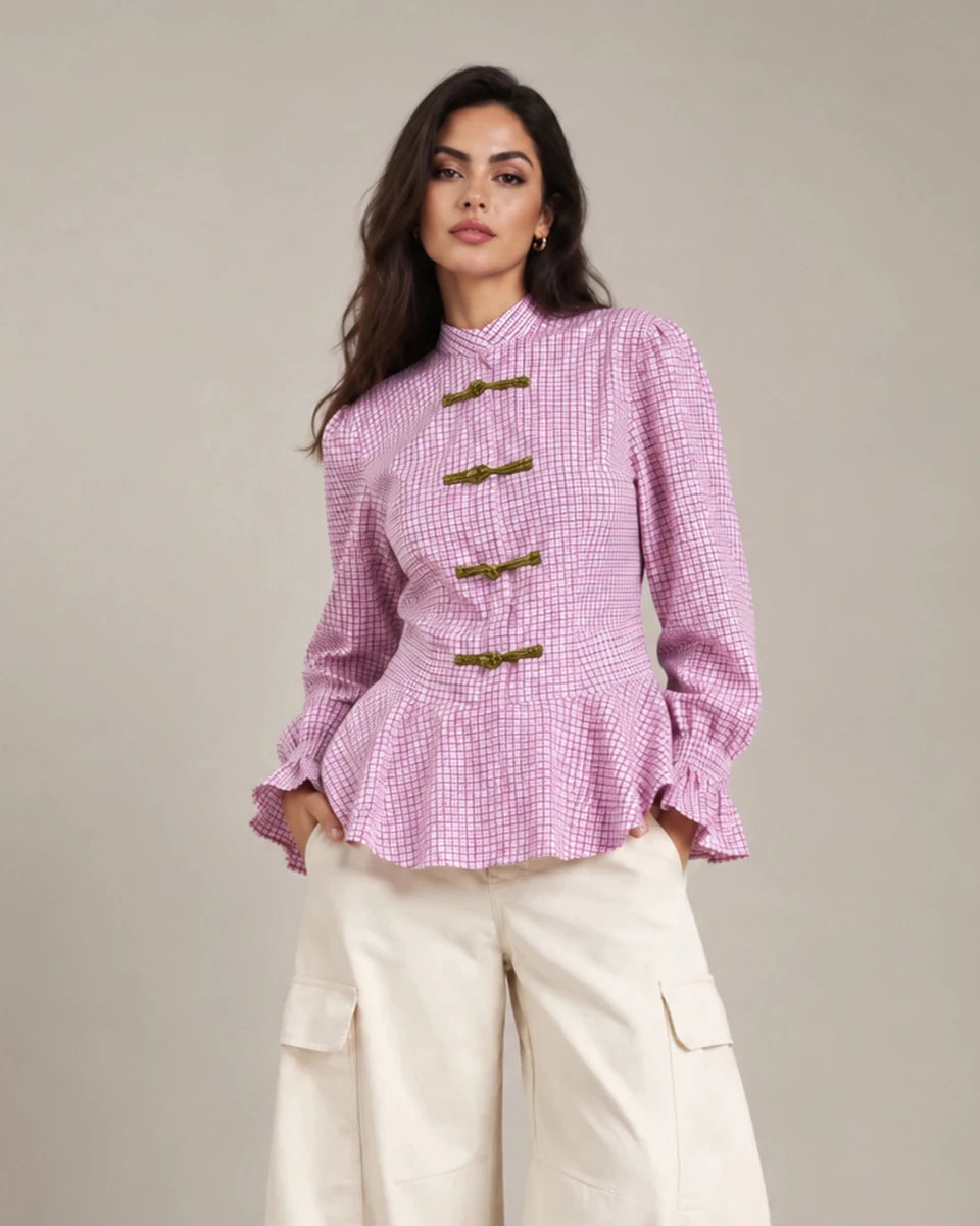 Close-up of the pink Regina check peplum shirt showing its decorative frog closures, peplum hem and ruffled cuffs.