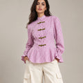 Close-up of the pink Regina check peplum shirt showing its decorative frog closures, peplum hem and ruffled cuffs.