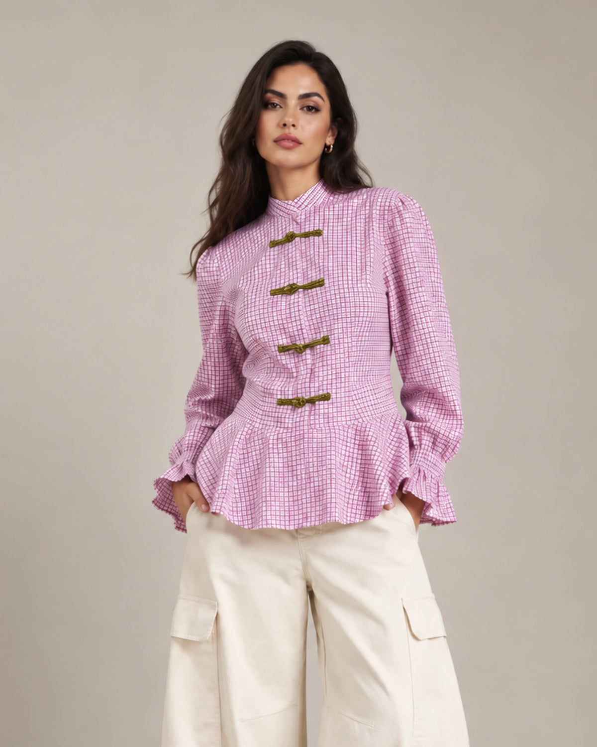 Close-up of the pink Regina check peplum shirt showing its decorative frog closures, peplum hem and ruffled cuffs.