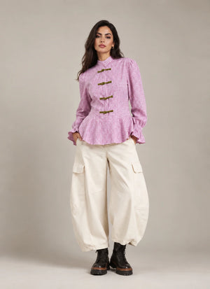 Full-length view of the pink Regina check peplum shirt with decorative frog closures, styled with ivory Vittoria Panna cargo balloon trousers.