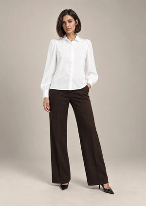 Full-length styling view of the white Serena shirt with a pointed collar and long puff sleeves, worn with brown wide-leg trousers.