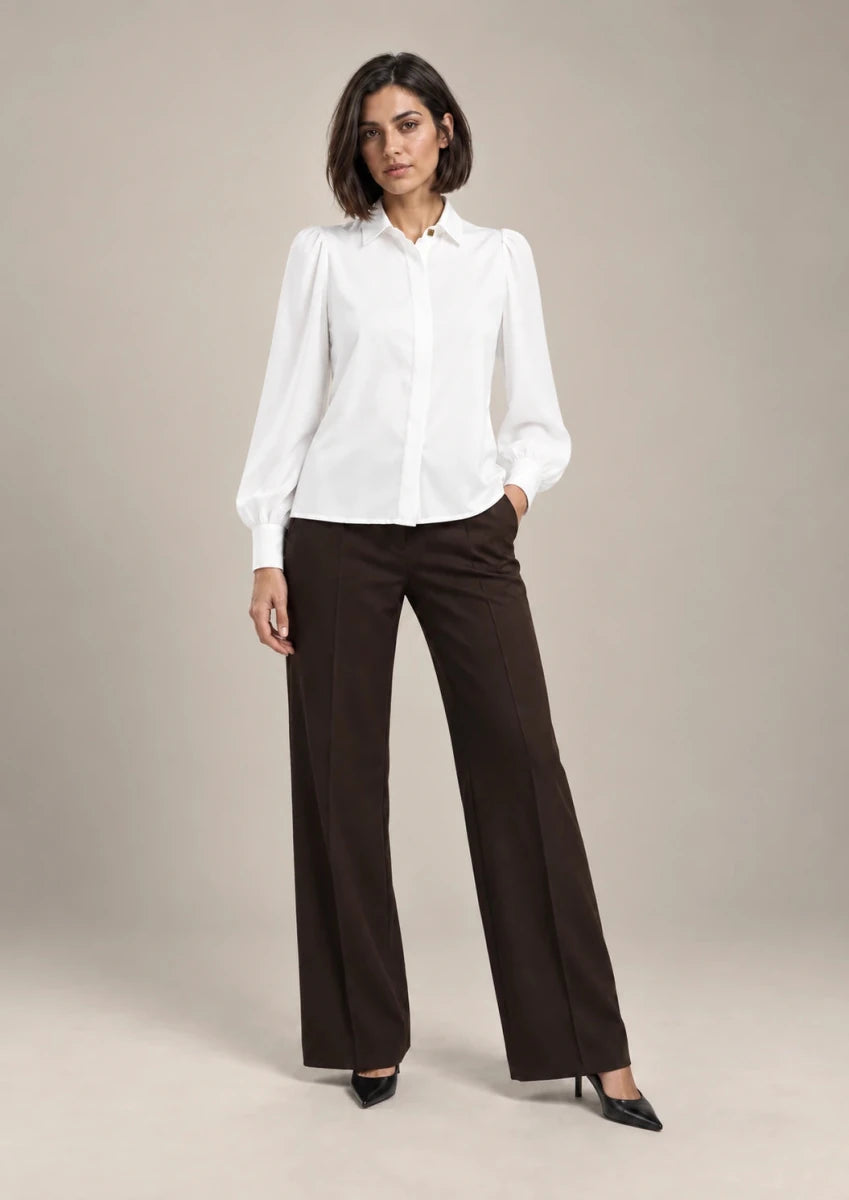 Full-length styling view of the white Serena shirt with a pointed collar and long puff sleeves, worn with brown wide-leg trousers.